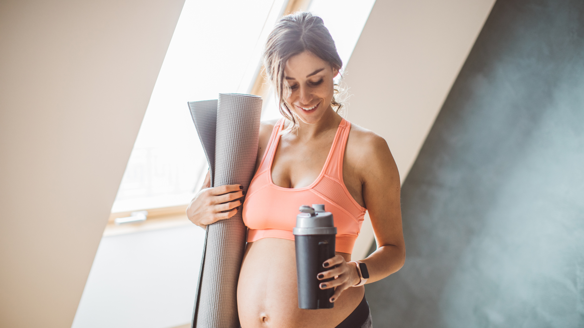 A pregnant lady is wearing a fitness outfit and getting ready to do some yoga.