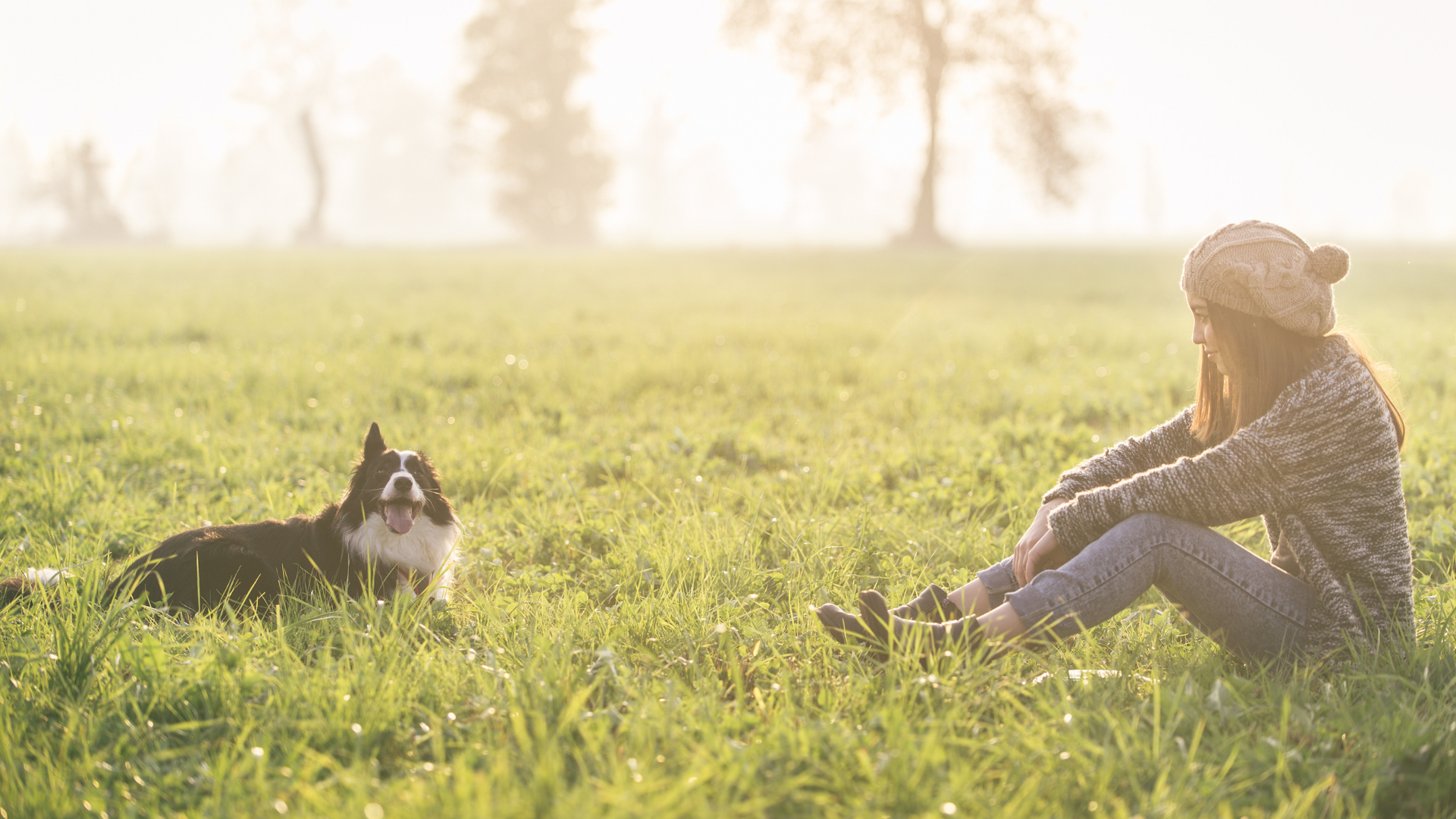 A woman sitting in a grassy field with her dog, finds time for self reflection. 