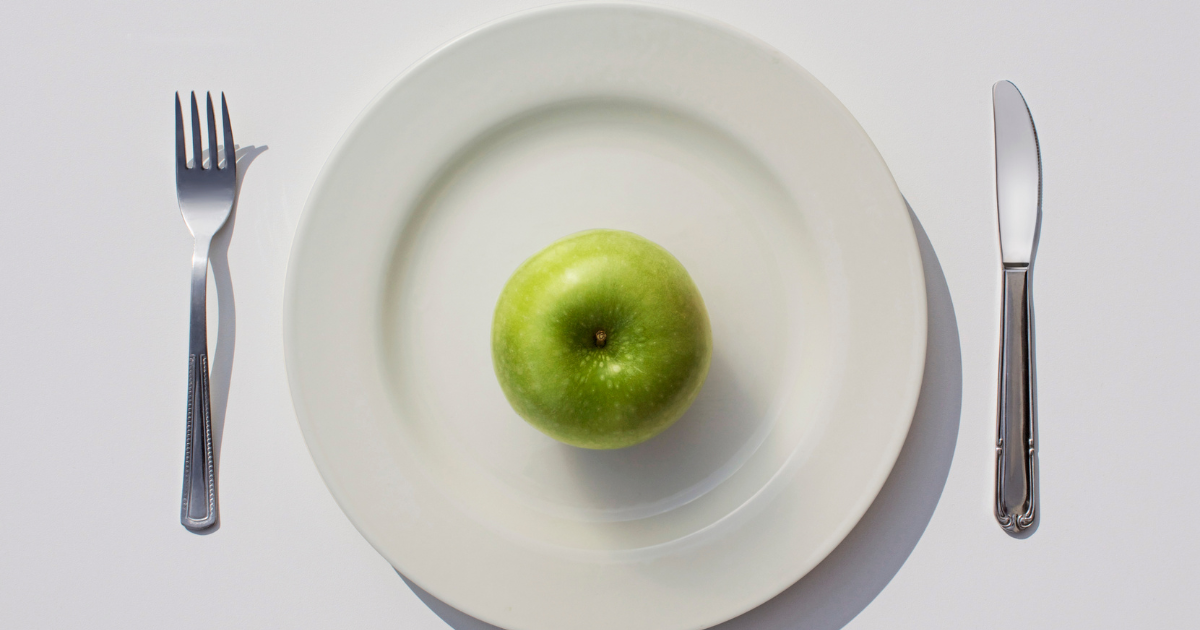 A single green apple sits on top of a plate symbolizing the diet culture we are exposed to every day. 