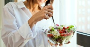 a woman is eating a brightly colored salad and smiling.